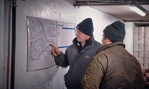 Two farmers pointing at a map on the wall